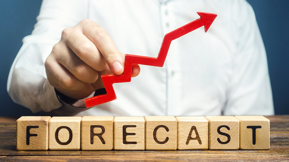 Man holds a red arrow up over wooden letter blocks which spell the word "forecast".